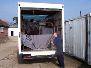 Two uniformed removal men loading wrapped furniture into a removals van